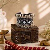 Oxidized silver ghungroo cuff bracelet on pink velvet bracelet stand draped in blush satin fabric, close-up showing mirror tiles, rhinestone clusters and triple ghungroo ball rows