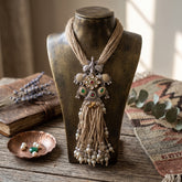 Long tribal elephant pendant necklace with natural-tone strands and pearl-like tassels on a display stand