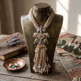 Long tribal elephant pendant necklace with natural-tone strands and pearl-like tassels on a display stand