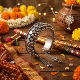 Oxidized silver ghungroo mirror cuff bangle on marigold garland Navratri flat lay with fairy lights, dandiya sticks, Kutchi dupatta and clay pot, warm festive styled shot showing full bangle and chain tassel