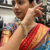 Indian model in silk saree wearing dual tone gold silver filigree triangle ghungroo bracelet, wrist raised to ear in elegant pose, jewellery store background