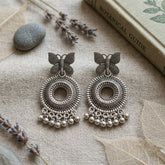 Pair of oxidized silver butterfly chandbali earrings with ghungroo drops on linen flat lay with lavender and botanical book