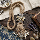 Two-tone elephant pendant necklace with jute-style strands and pearl-like tassels on a rustic background