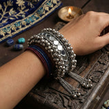 Both wrists of Indian model in pink patola Navratri outfit with henna hands wearing matching pair of oxidized silver ghungroo mirror cuff bangles, arms crossed showing stackable styling and chain tassel drops
