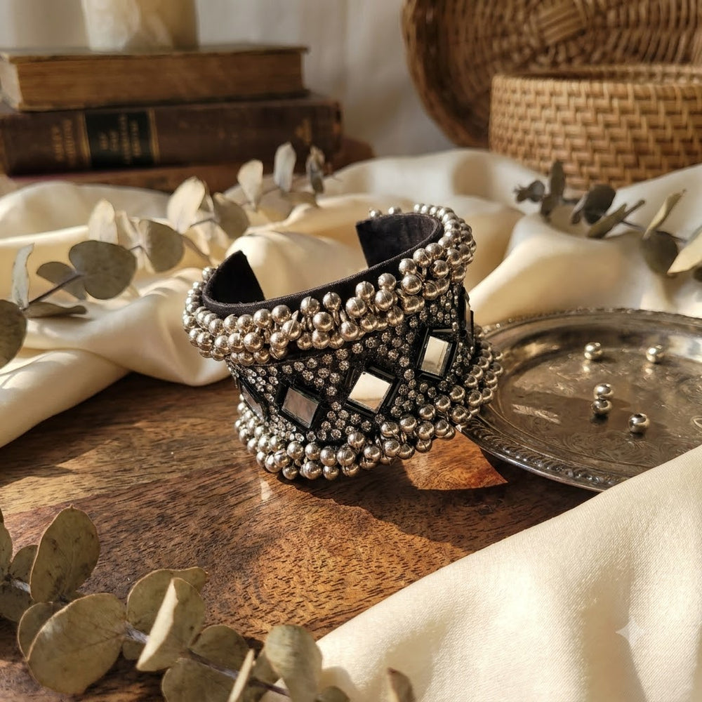 Oxidized silver mirror work ghungroo cuff bracelet displayed on carved wooden elephant jewellery box with brass diyas, dandia sticks and white babys breath flowers, heritage Indian flat lay