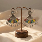 Pair of oxidized silver garba dancer meenakari earrings with ghungroo drops displayed on wooden earring stand