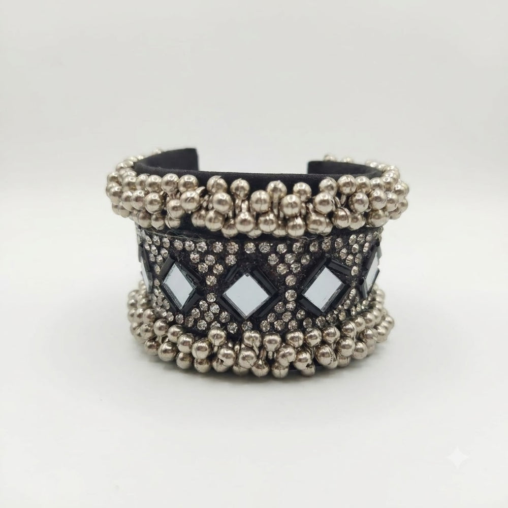 Close-up of hand wearing oxidized silver mirror work ghungroo cuff bracelet, white background, showing full cuff structure and ghungroo ball fringe detail