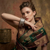 Indian woman in black mirror-work embroidered chaniya choli with pink dupatta wearing silver wide filigree bangle with ghungroo drops, wrist raised close-up showing full bangle detail with Diwali bokeh lights