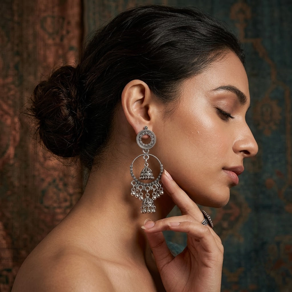 Indian model touching face while wearing oxidized silver double hoop chandbali earrings, vintage background portrait