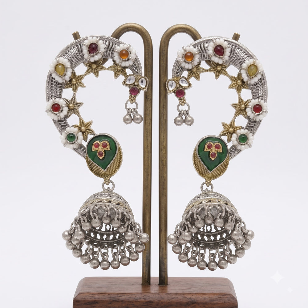 Pair of dual tone Navratna floral ear cuff jhumka earrings displayed on antique brass stand with white background, showing both left and right pieces with white enamel flowers, coloured gemstone centres, gold star motifs, green meenakari heart pendant and full filigree jhumka with pearl ghungroo fringe