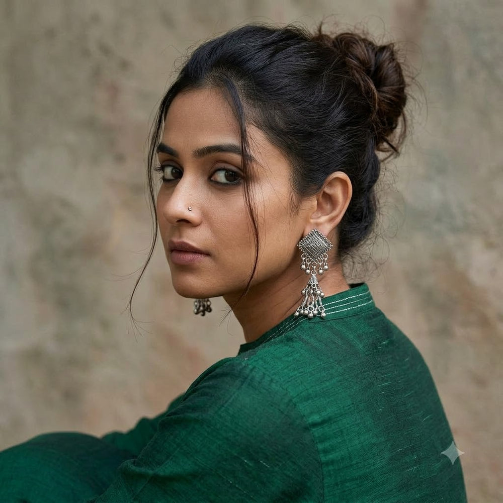 Indian model in forest green kurta wearing oxidized silver diamond square jhumka earrings, artistic over-shoulder portrait with bun updo