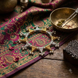 Dual tone gold silver filigree triangle ghungroo bracelet on magenta green Banarasi brocade with brass singing bowl, saffron and cardamom spices, heritage Indian flat lay