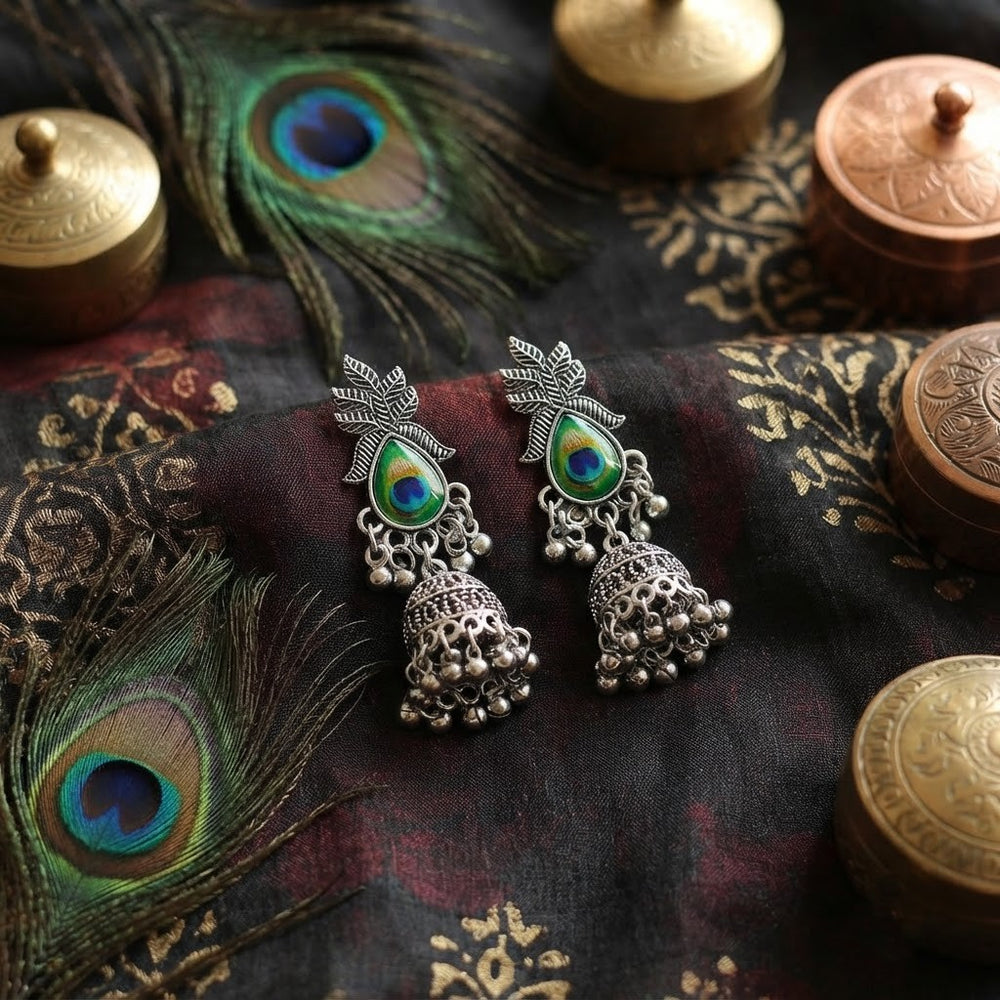 Oxidized silver peacock jhumka earrings on dark aesthetic background with peacock feathers
