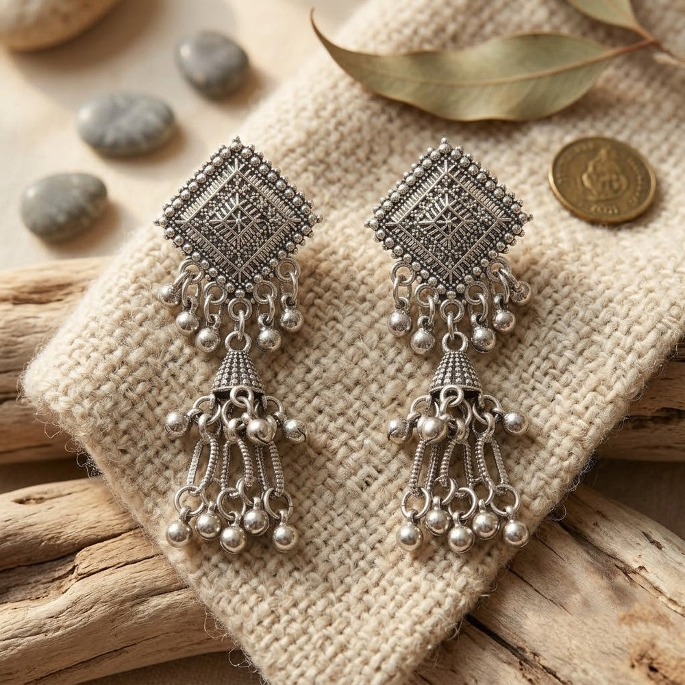 Oxidized silver diamond square chandelier jhumka earrings on rust red fabric with star anise, pearl string and teal brocade flat lay