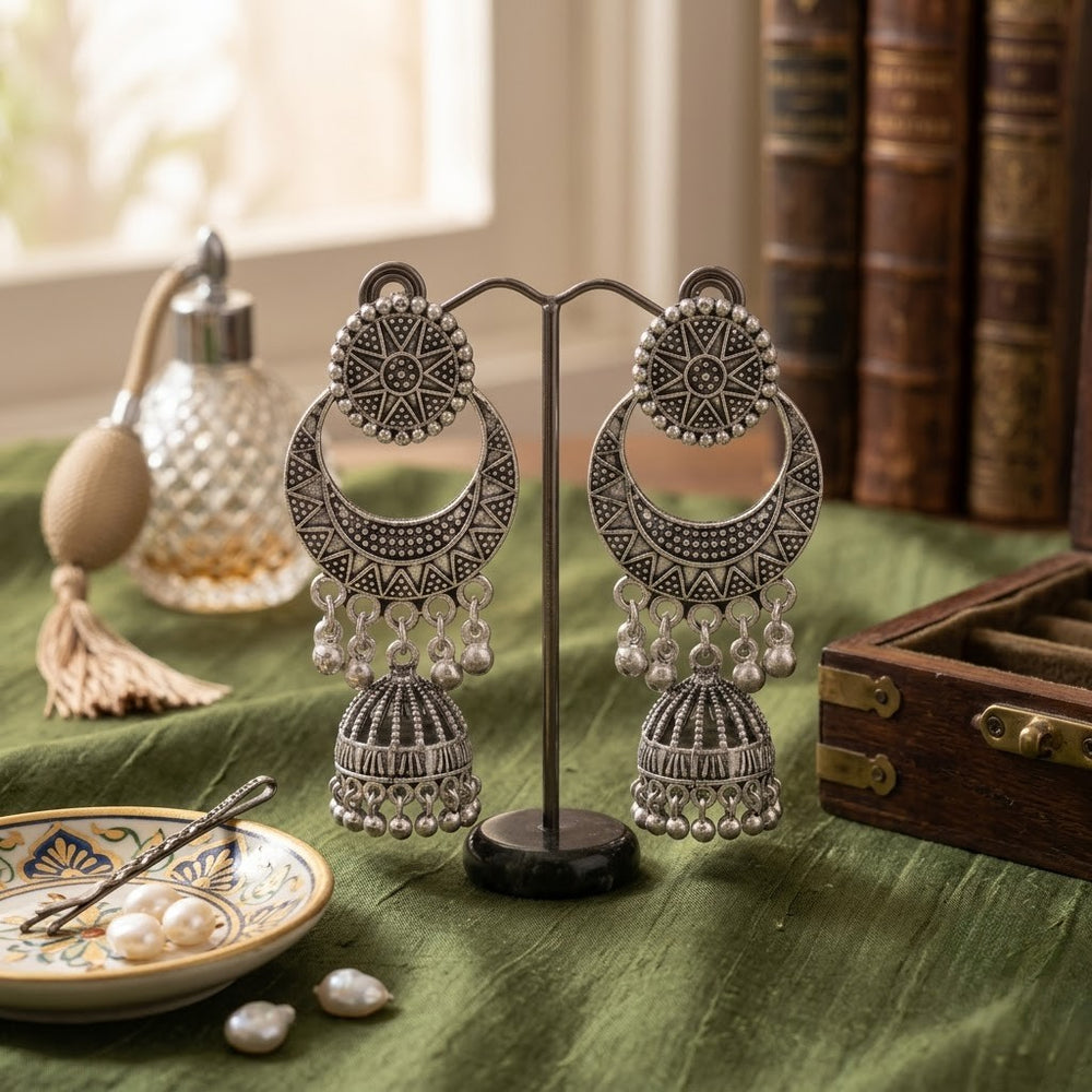 Oxidized silver chandbali jhumka earrings on dark carved wooden tray with indigo fabric, dried petals and turquoise beads flat lay