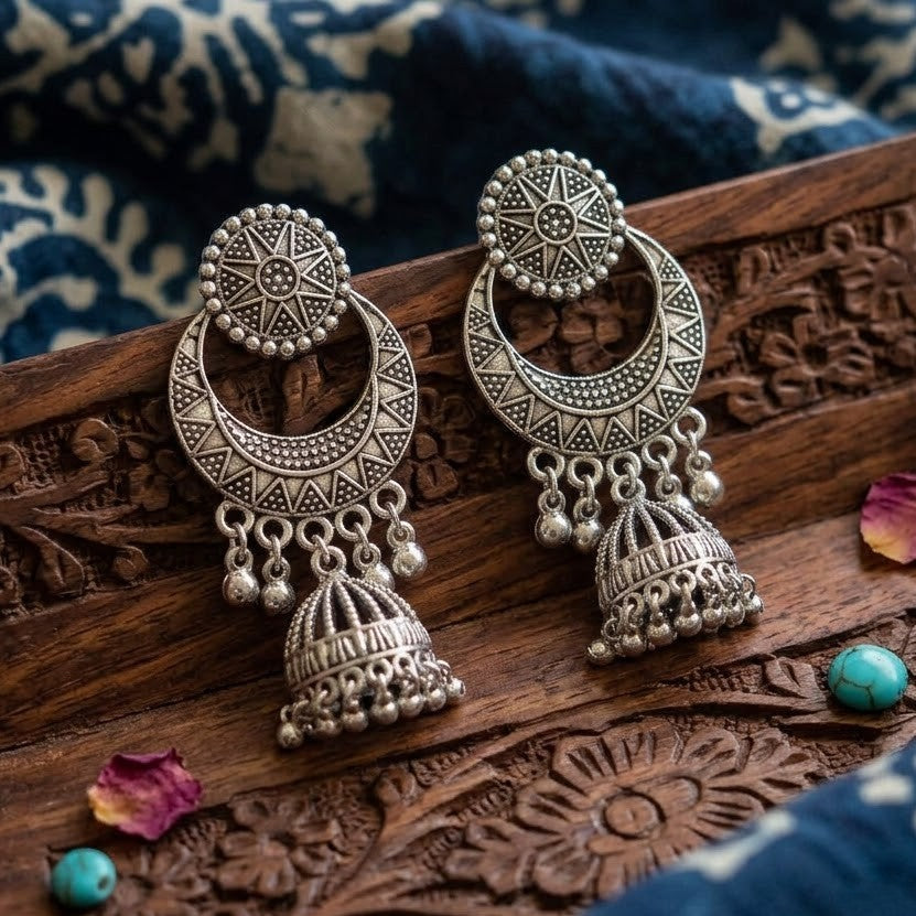 Oxidized silver chandbali jhumka earrings reflected in vintage brass hand mirror with model smiling outdoors