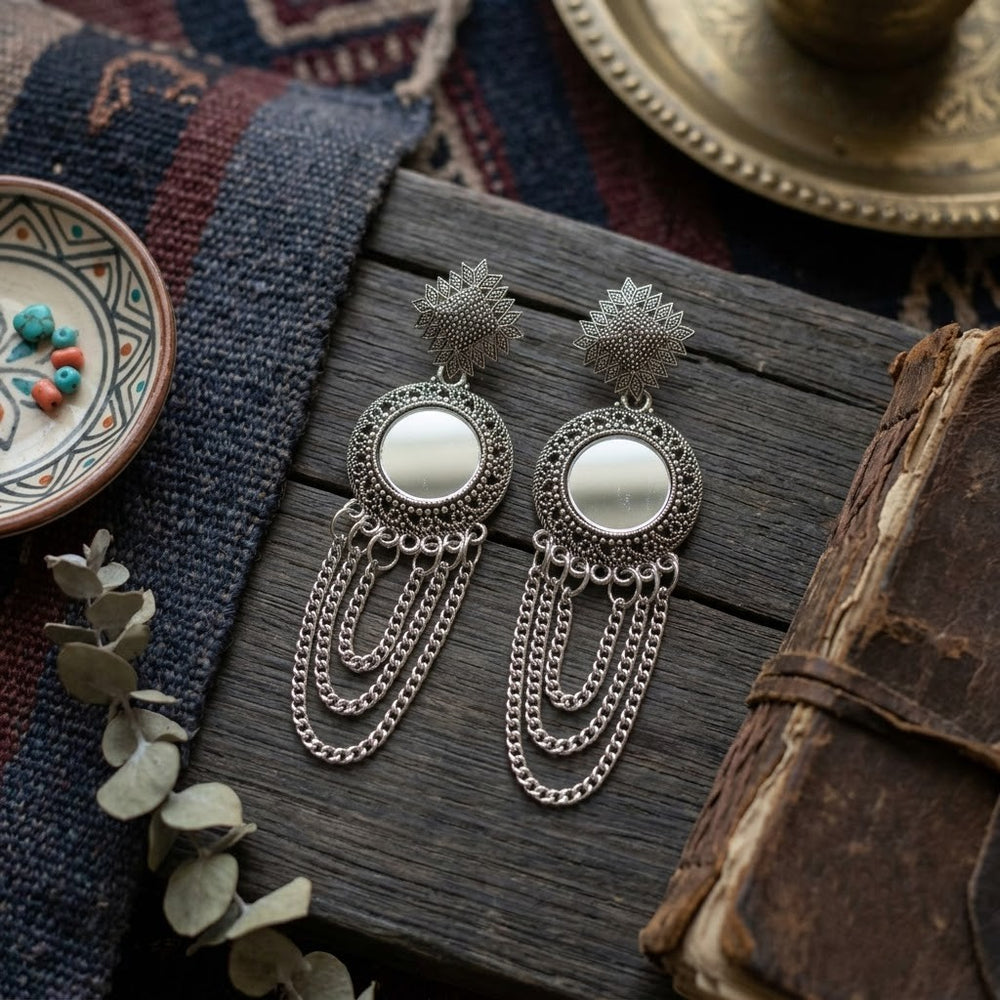 Oxidized silver mirror chandelier earrings styled on rustic wooden surface with coloured beads and vintage book