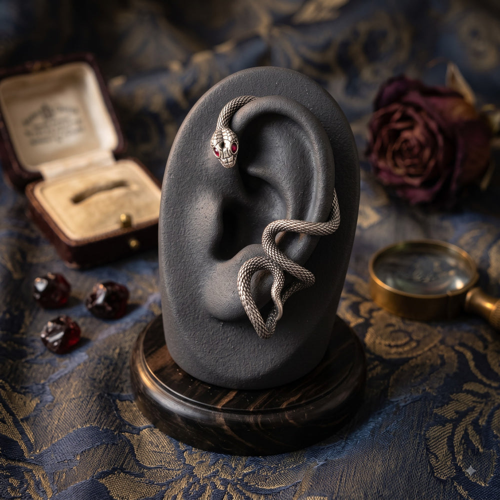 Second view of oxidized silver snake ear cuff with red eye on bronze ear mannequin, slightly different angle showing full serpent coil wrap from helix to lobe with tail curl and red eye detail
