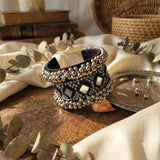 Oxidized silver mirror work ghungroo cuff bracelet displayed on carved wooden elephant jewellery box with brass diyas, dandia sticks and white babys breath flowers, heritage Indian flat lay