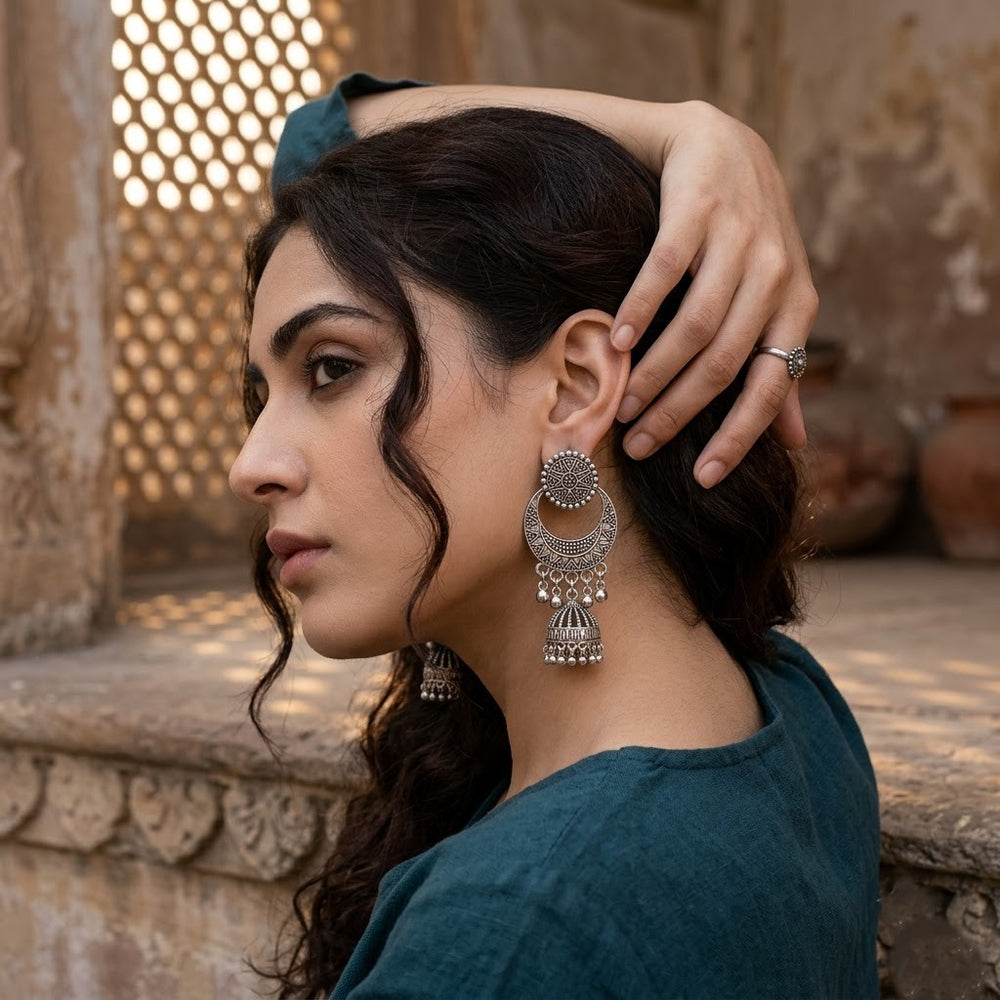 Indian model with curly hair wearing oxidized silver chandbali jhumka earrings in front of heritage jali architecture, teal kurta