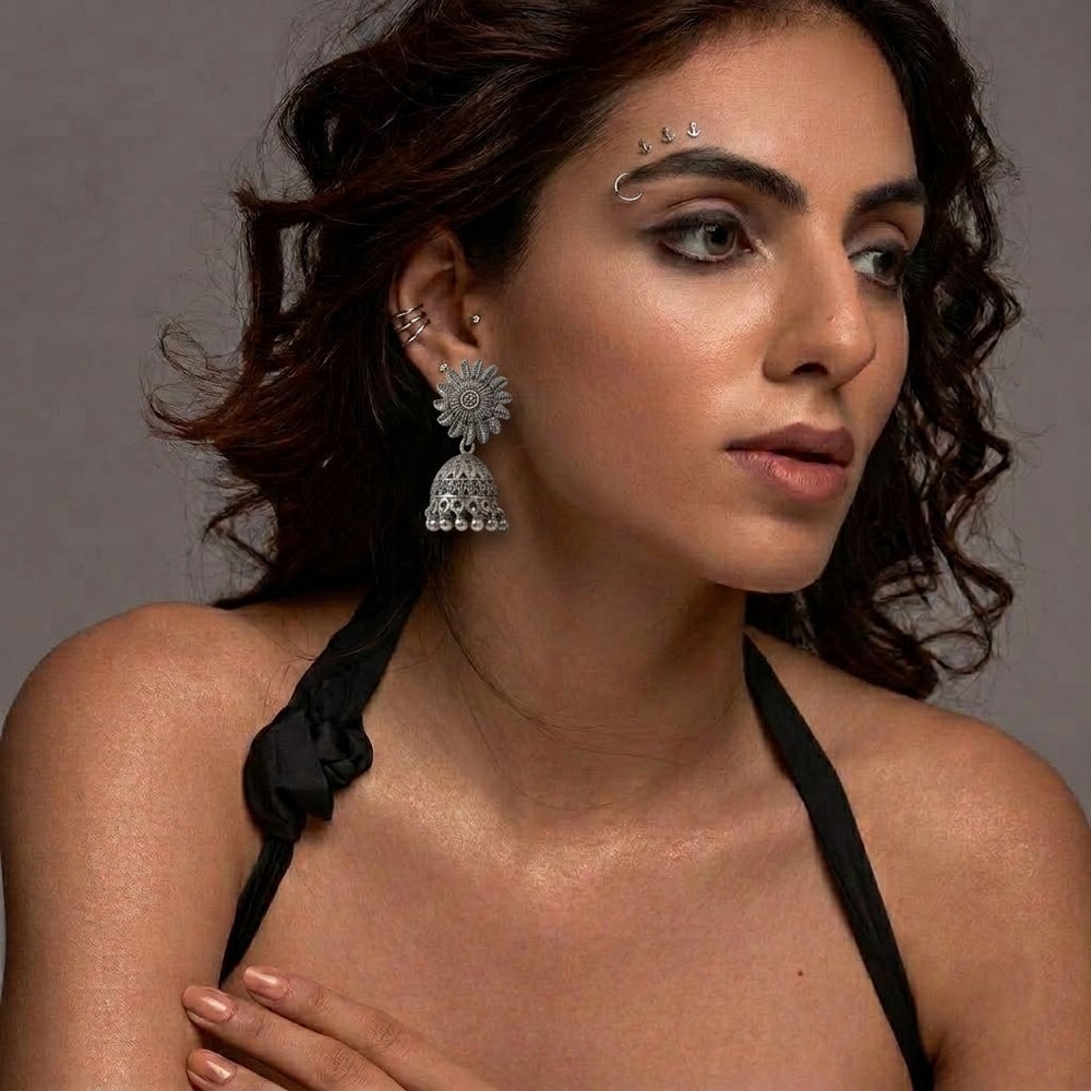 Indian model wearing oxidized silver sunflower jhumka earrings with dark curly hair, grey studio background, editorial look