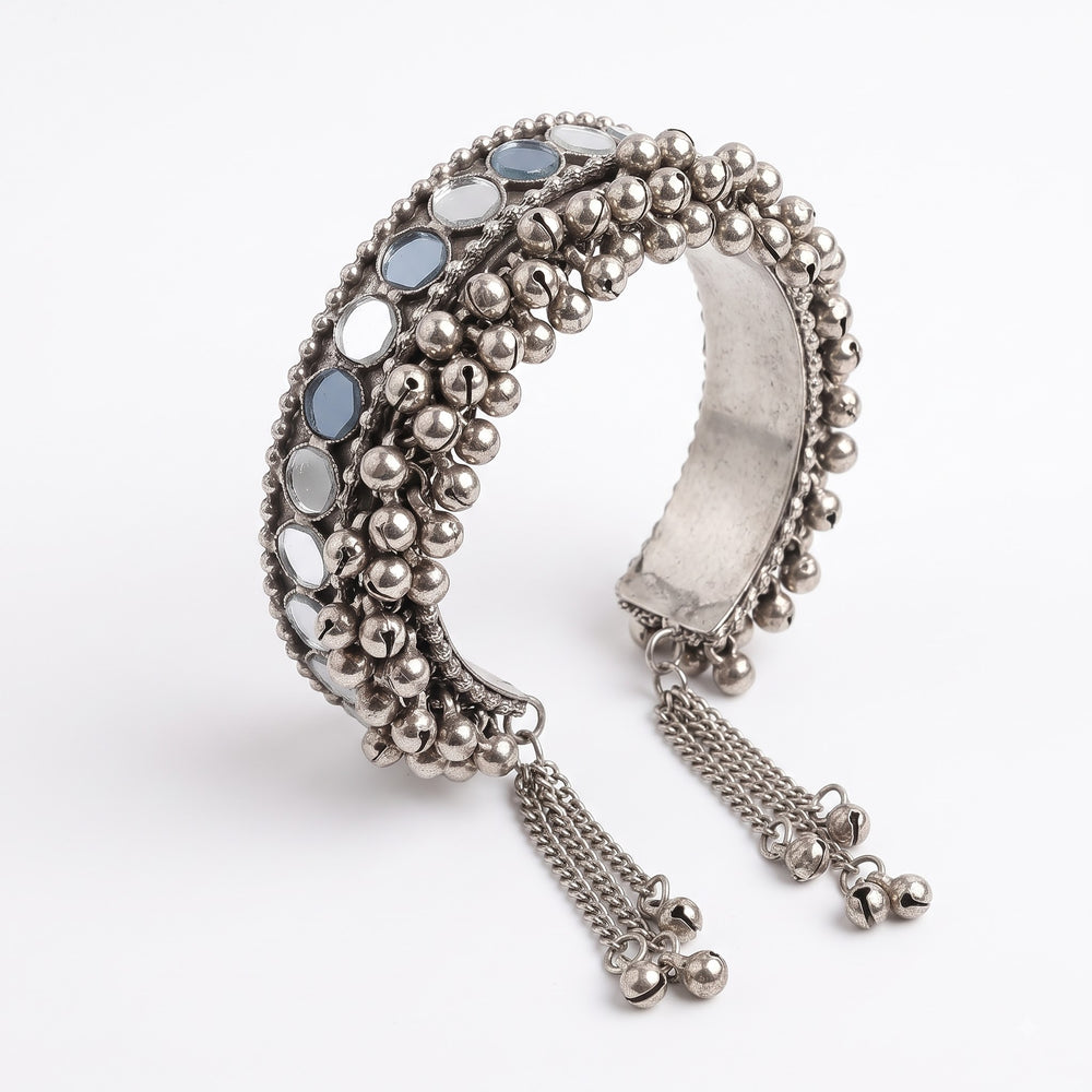 Oxidized silver mirror work ghungroo cuff bangle with chain tassel on plain white background, front view showing full dense ghungroo ball surface, twin rows of oval mirror tiles and hanging chain tassel with bell drops