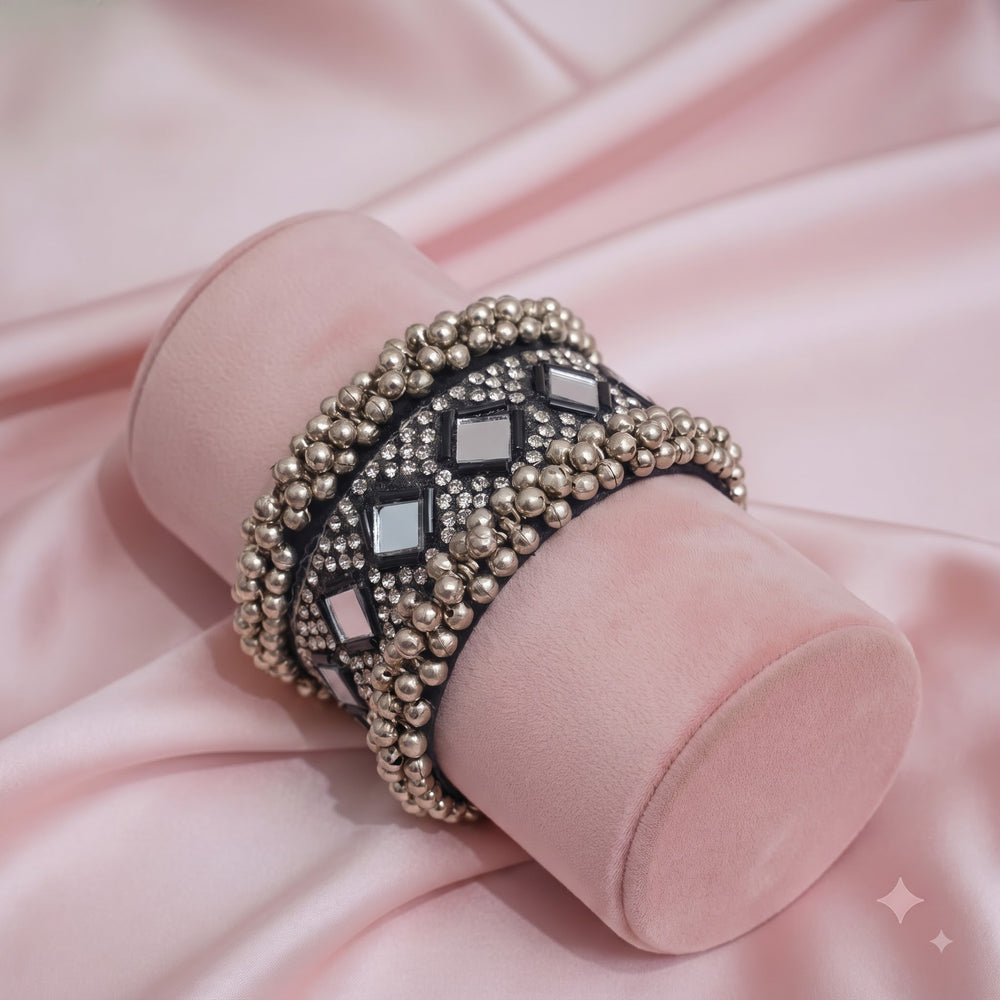 Oxidized silver mirror work ghungroo cuff bracelet on carved wooden elephant jewellery box with brass diyas and dandia sticks, alternate angle flat lay