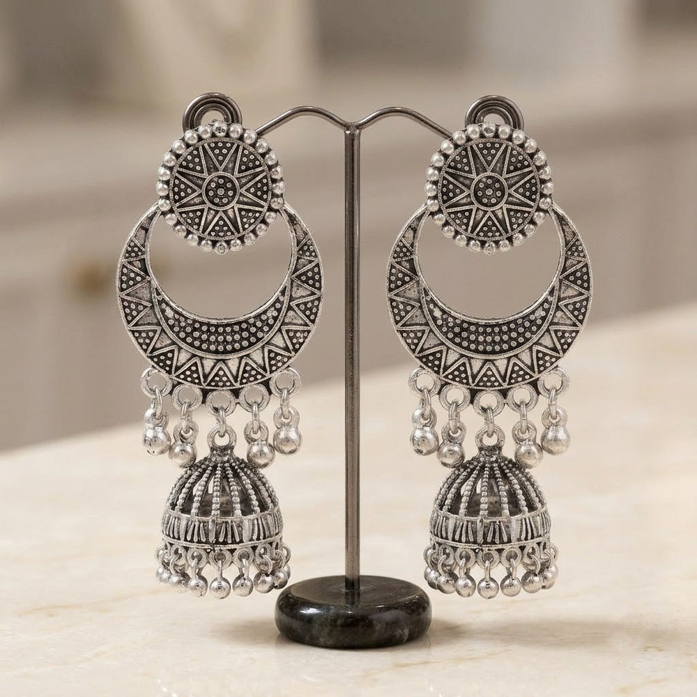 Pair of oxidized silver sunburst chandbali jhumka earrings displayed on silver earring stand, marble surface