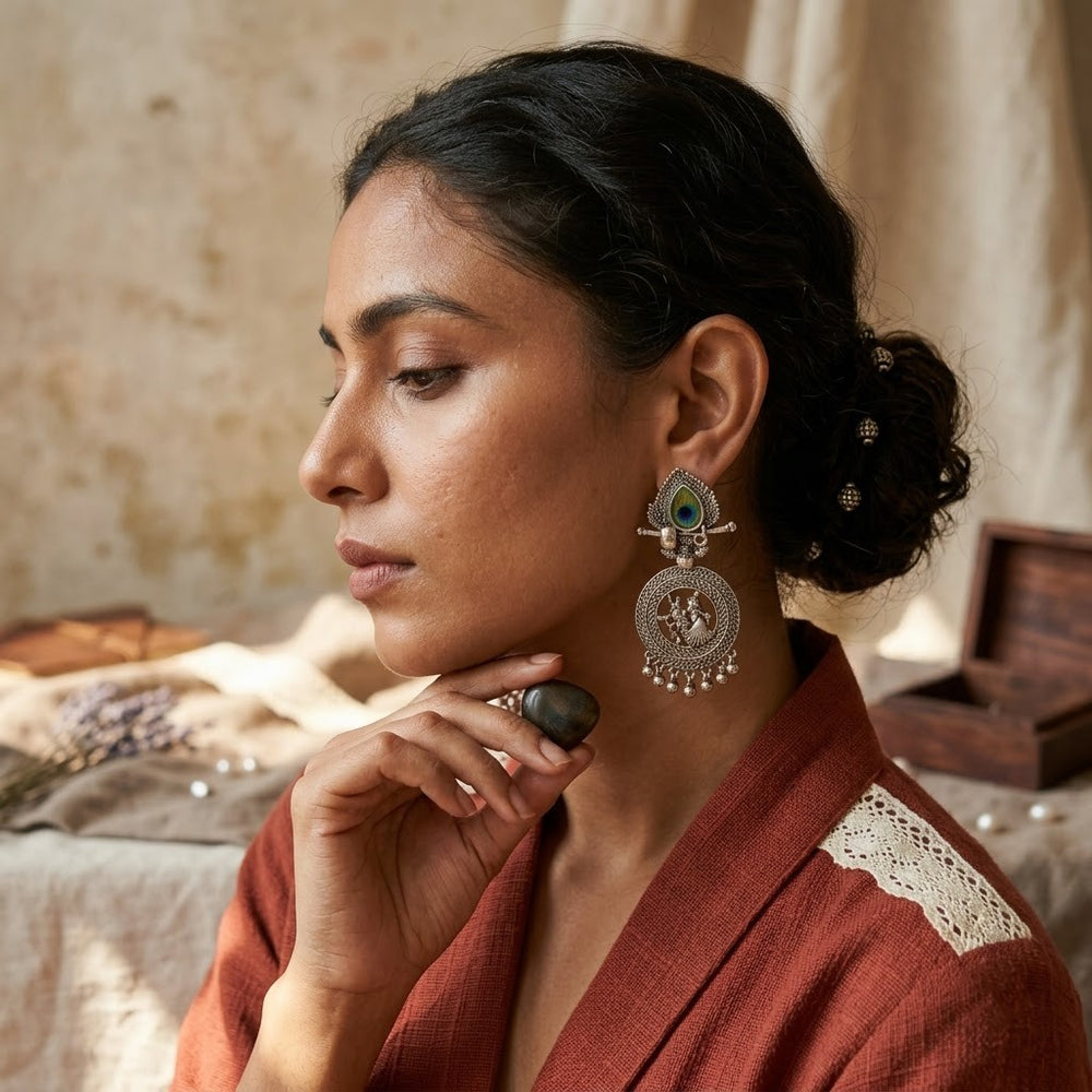 Model wearing oxidized silver Radha-Krishna chandbali earrings, editorial close-up, rust red dupatta