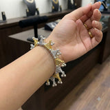 Close-up of hand wearing dual tone gold silver triangle ghungroo charm bracelet, palm open showing full bracelet structure and ghungroo drops, jewellery store background