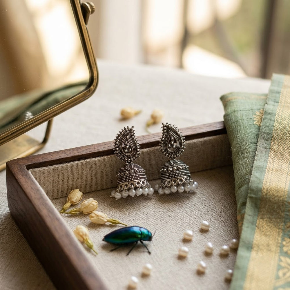 Oxidized silver paisley jhumka earrings in wooden tray with jasmine flowers and green silk saree