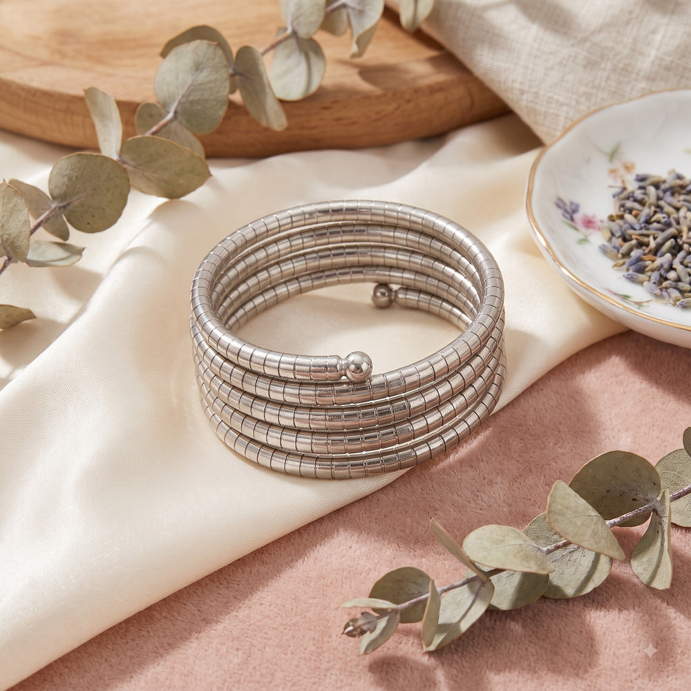 Silver oxidized 5-coil snake wrap bracelet on wrist with lavender sprig, gold-rim tea cup, burning candle and leather books in soft morning light aesthetic flat lay