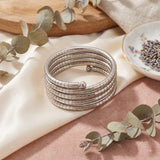 Silver oxidized 5-coil snake wrap bracelet on wrist with lavender sprig, gold-rim tea cup, burning candle and leather books in soft morning light aesthetic flat lay