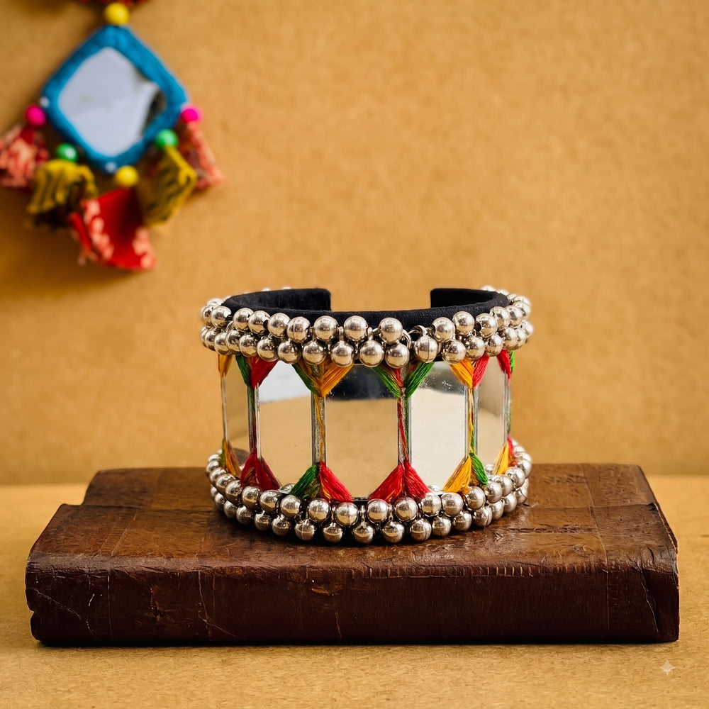 Indian model in yellow chaniya choli with cowrie choker necklace and jhumka earrings wearing large mirror tile ghungroo cuff bracelet, seated on stone steps in full Navratri festive look