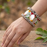 Smiling Indian model in black top with hair down wearing large mirror tile ghungroo cuff bracelet, hand raised near face against old wooden door in outdoor natural light portrait