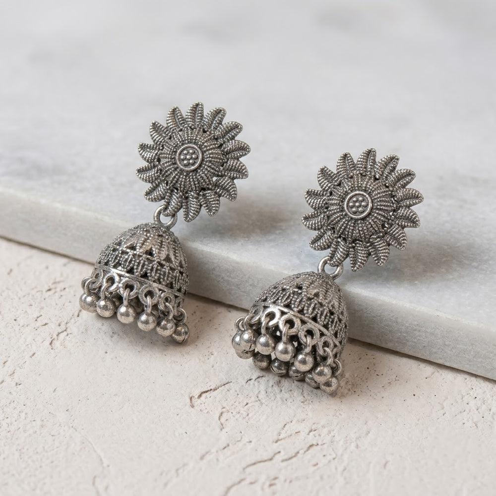 Pair of oxidized silver sunflower jhumka earrings leaning on white marble surface, clean product shot
