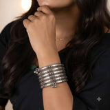 Indian model in dark outfit wearing silver oxidized snake coil wrap bracelet, close-up moody portrait with hands raised near face showing bracelet detail and ghungroo charm