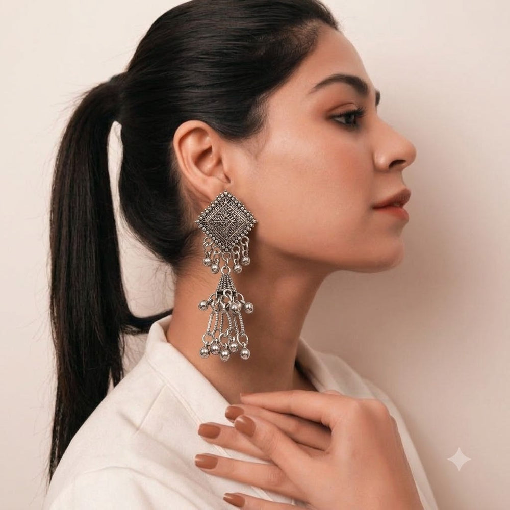 Indian model in white shirt wearing oxidized silver diamond square chandelier jhumka earrings, elegant side profile with ponytail, beige background